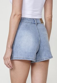 Svetlo modri jeans kratke hlače z visokim pasom, z neobdelanim robom in subtilnim zbledanjem. Imajo blagovno znamko iz usnja na zadnjem pasu.