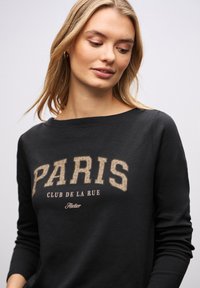 Sort sweatshirt med vid halsudskæring, der har et stort "PARIS"-tryk i beige med et tekstureret mønster og mindre tekst under.