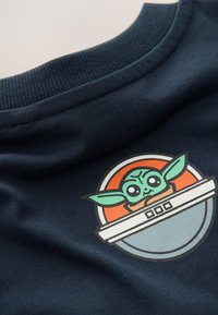 Navy T-shirt collar with a soft texture, featuring a colorful circular graphic of a character with large ears and expressive eyes.