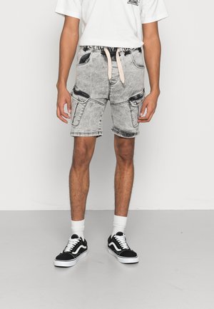 Pantaloni corti di jeans grigi chiari con vita con cordoncino, due tasche laterali e dettagli sbiaditi sottili, abbinati a sneakers nere e calzini bianchi.
