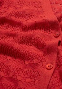 Červený pletený svetr s krajkovým vzorem, texturovaným materiálem a zapínáním na knoflíky. Knoflíky jsou kulaté a jasně červené.