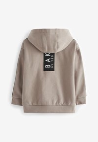 Beige huppari, jossa on suuri musta tarra, jossa lukee "BAK BY TED." Varustettu hupulla, ribbausvanteilla ja mustilla sivupaneeleilla. Pehmeä pinta.