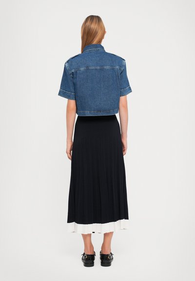 Kuttet denimjakke med korte ermer; designet i mørkeblå. Kombinert med et plisserte marineblått skjørt med hvit kant og svarte sko.