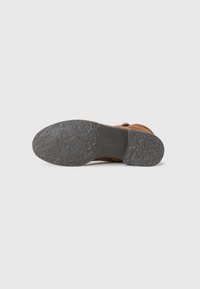 Semelle de chaussure en cuir marron avec un grip texturé, dotée d'une semelle extérieure en caoutchouc gris avec un motif et un logo de marque en relief.