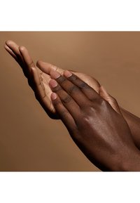 Zwei Hände, eine helle und eine dunkle, verbunden mit den Handflächen, die glatte Hauttexturen und kurze, natürliche Nägel präsentieren, vor einem neutralen Hintergrund.