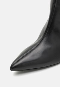 Svarte skinn ankelstøvler med spiss tå, glatt tekstur, minimal søm og en tettsittende design. Ingen synlig maskinvare eller accenter.