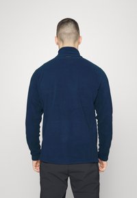 Tamsiai mėlyna vilnos puloveris su aukštu apykakle, ilgomis rankovėmis ir elastingais manžetais. Yra mažas logotipas ant kaklo nugaros ir glotnus paviršius.