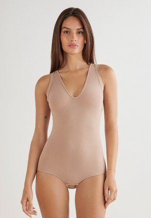 Beżowy bodysuit z prążkowanego materiału, z głębokim dekoltem w kształcie V, szerokimi ramiączkami i dopasowanym krojem. Miękka tekstura i bezszwowa konstrukcja zwiększają komfort.
