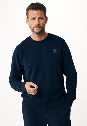 Marineblå sweatshirt lavet af blødt stof, med en rund udskæring, ribbede manchetter og et lille logopatch på den øverste venstre bryst.