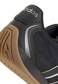 Talons de baskets Adidas noires avec semelle en caoutchouc naturel, logo Adidas argenté sur le côté et languette perforée noire au talon.