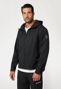 Juoda užtrauktuku užsegama striukė su kapišonu, pagaminta iš glotnaus, lengvo audinio. Yra raišteliai, logotipas ant rankovės ir elastingi rankogaliai.