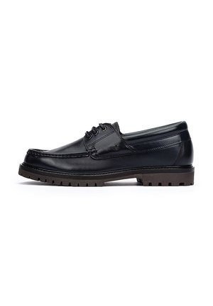 Zapato náutico de cuero negro con corte bajo, punta redonda, diseño con cordones y suela de goma marrón resistente. Presenta costuras decorativas y acentos sutiles.