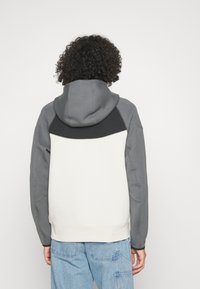 Felpa con cappuccio grigia, nera e bianca. Presenta una tasca a marsupio, polsini a costine e un design a blocchi di colore con tessuto testurizzato.