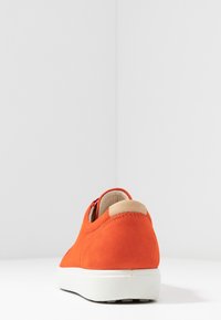 Zapatillas de ante naranja con suela blanca, de forma redondeada y acento beige en el talón. Textura suave y detalles de costura visibles.