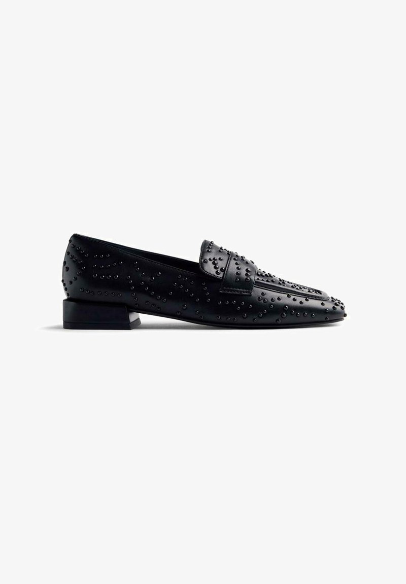 Mocassins en cuir noir avec un design texturé et des clous en relief. Talon bas et bout arrondi. Surface lisse avec des accents détaillés.