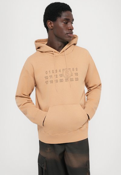 Huva sweatshirt i mjukt beige tyg med ett grafiskt tryck av siffror och en cirkulär logotyp över bröstet. Inkluderar en känguruficka.