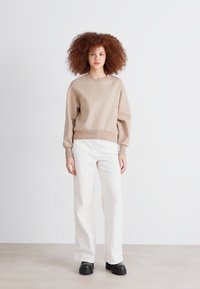 Beige genser med rund hals og ballongsærmer, kombinert med hvite vide bukser og svarte platåsko. Strukturert stoff.