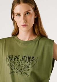 T-shirt senza maniche di colore verde oliva con scollo rotondo, caratterizzata da una stampa grafica nera di ali e il testo "PEPE JEANS LONDON" e "SINCE 1973."