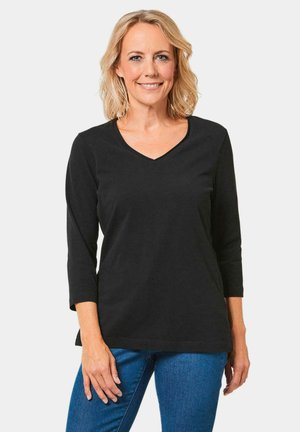 Zwarte lange mouwen V-hals top van zachte stof, met een ontspannen pasvorm en subtiele zijsplitsingen, gecombineerd met blauwe jeans.