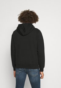 Felpa nera con cappuccio e vestibilità comoda, caratterizzata da un tessuto testurizzato, polsini e vita a coste, abbinata a jeans in denim blu.