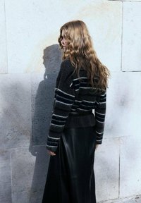 Maglione a maglia scura con righe orizzontali grigie e blu, abbinato a una gonna in pelle nera. Texture liscia, vita aderente e maniche lunghe.