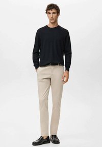 Maglione nero a maniche lunghe, pantaloni beige aderenti, mocassini neri. Tessuto liscio, design semplice, senza motivi o dettagli visibili.