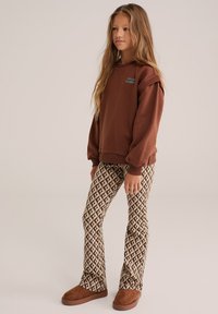 Brun sweatshirt med ribbad nederkant, med blå broderad text. Mönstrade bruna och beige vida leggings med diamantsymboler. Bruna slip-on skor.