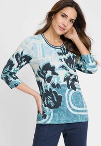 Bloemmotief top in lichtblauw en zwart, voorzien van driekwartmouwen, ronde halslijn en een mix van texturen en grafische ontwerpen.