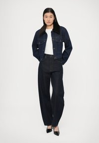 Temno modra jeans jakna z ovratnikom iz umetnega kožuha, kombinirana z visokim pasom temne jeans hlače, ki ustvarjajo oprijet silhueto. Obleko dopolnjujejo črni visoki petke.