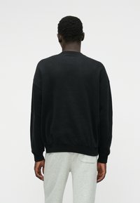 Μαύρη φόρμα με χαλαρή εφαρμογή, στρογγυλή λαιμόκοψη, ριμπ μανίκια και στρίφωμα. Υφασμάτινη από βαμβάκι, ορατές ραφές και χωρίς γραφικά.