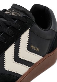 Baskets noires avec une tige en daim texturée, un motif beige en zigzag, le texte doré "VM78 CPH" et une semelle en caoutchouc marron.