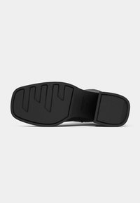 Semelle de chaussure noire à design plat, avec des motifs striés pour la traction et une surface lisse. Matériau durable avec des accents minimaux.