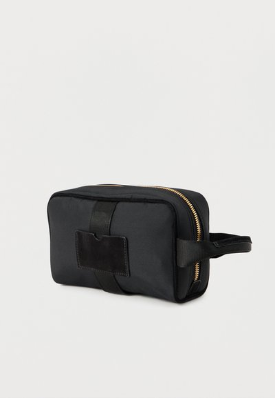 Μαύρο νάιλον νεσεσέρ με χρυστό φερμουάρ, ορθογώνιο σχήμα, υφή στην επιφάνεια, με πλαϊνή λαβή και κατακόρυφο δερμάτινο διακοσμητικό.