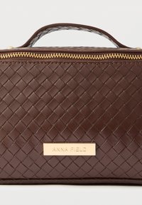 Ruda pintos odos rankinė su plokščia forma, auksiniu užtrauktuku ir metaline logotipo plokštele. Viršuje yra nešiojimo rankena patogiam nešiojimui.