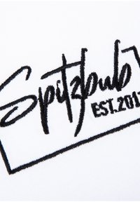 Weißer Stoff mit schwarzem gesticktem Text, der "Spitzbub" und "EST.2017" innerhalb eines rechteckigen Rahmens zeigt.