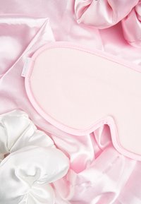 Rosa satinöga med mjuka rundade kanter, omgiven av vita satin scrunchies på en rosa satinbakgrund.