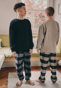 To drenge iført afslappet tøj: den ene i en sort langærmet trøje, den anden i en lysegrå trøje. Begge har ternede flannelbukser på.