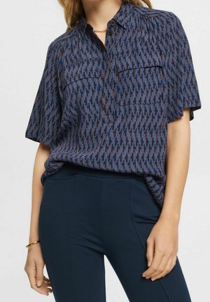 Short-sleeve navy blouse with a multicolored abstract pattern, two front pockets, and a classic collar. Smooth, lightweight fabric.