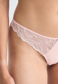 Lys rosa truser med en scalloped blonde midje og glatt stoff. Detalj viser blomstret blonde mønster langs kantene.