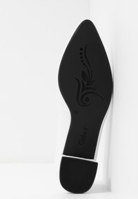Semelle d'une chaussure blanche à bout pointu avec talon texturé noir et semelle décorative noire ornée d'un motif floral et de la marque "Gabor".