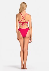 Jasnoróżowy bikini z krzyżującymi się ramiączkami i zapięciem na kokardę, z wysokimi bokami. Gładki, elastyczny materiał o minimalistycznym designie.
