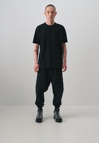 Black t-shirt with a relaxed fit, paired with loose black trousers featuring side pockets, and gray patterned shoes.