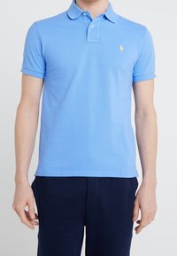 Ljusblå pikétröja i bomull med klassisk krage, korta ärmar och en broderad logotyp på vänster bröst.