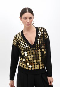Black sweater with a deep V-neck, adorned with circular gold sequins, featuring long sleeves and a fitted hem. Patterns vary in size.