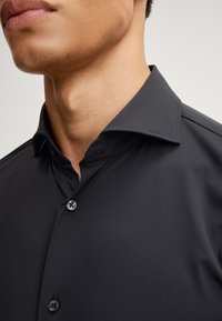Camicia nera realizzata in tessuto liscio con un design button-up, caratterizzata da un colletto a punta e bottoni neri abbinati.