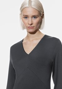 Grijze V-halsjurk met lange mouwen, gemaakt van een zachte stof, met een chevrondesign en strakke, minimalistische lijnen.