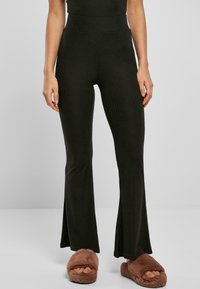 Leggings acampanados de canalé en verde oscuro con una cinturilla alta, que presentan una textura suave. Combinados con pantuflas de peluche marrones.