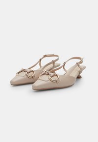 Beżowe syntetyczne buty slingback z pointed toe, z dekoracyjnym złotym elementem i paskiem na kostce. Gładka tekstura, niski obcas.