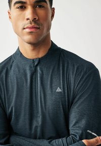 Dunkelgraues, langärmliges Sportshirt mit einem Halbzipp-Kragen und Logodetail. Hergestellt aus einem strukturierten, feuchtigkeitsableitenden Stoff.
