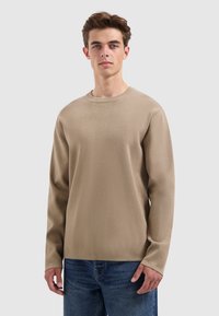 Beige langharige trui met een ronde hals en textuurstof, gecombineerd met blauwe jeans. Eenvoudig ontwerp, casual pasvorm en geen zichtbare patronen.
